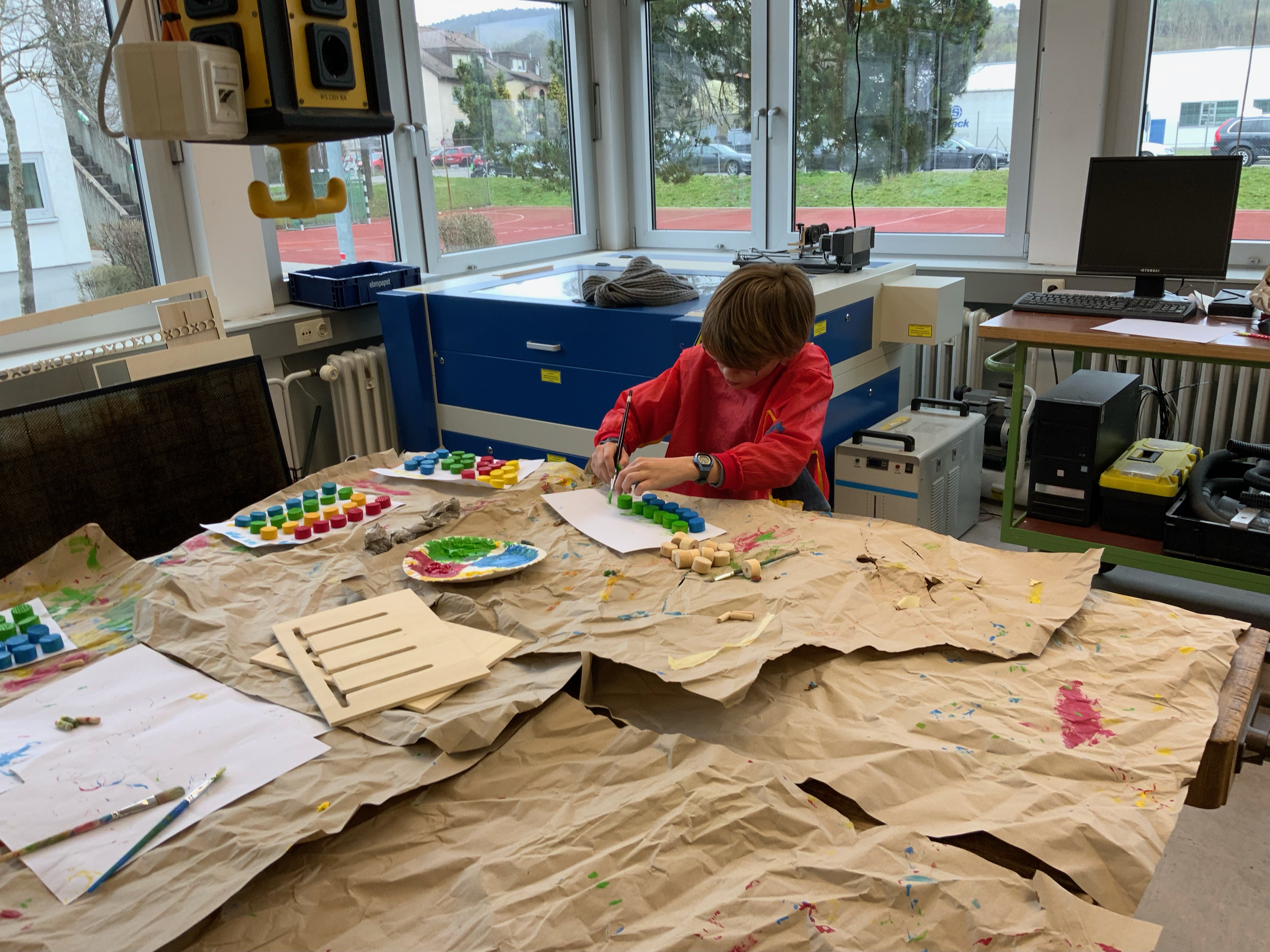 Ein Junge klebt konzentriert farbige Holzelemente auf ein Blatt